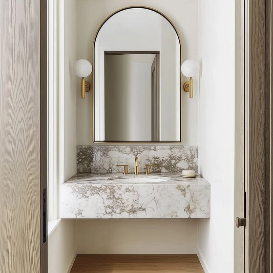 Elegant bathroom vanity with a marble countertop and backsplash, featuring an arched mirror, brass fixtures, and modern wall sconces, creating a luxurious and refined look in a minimalist space.